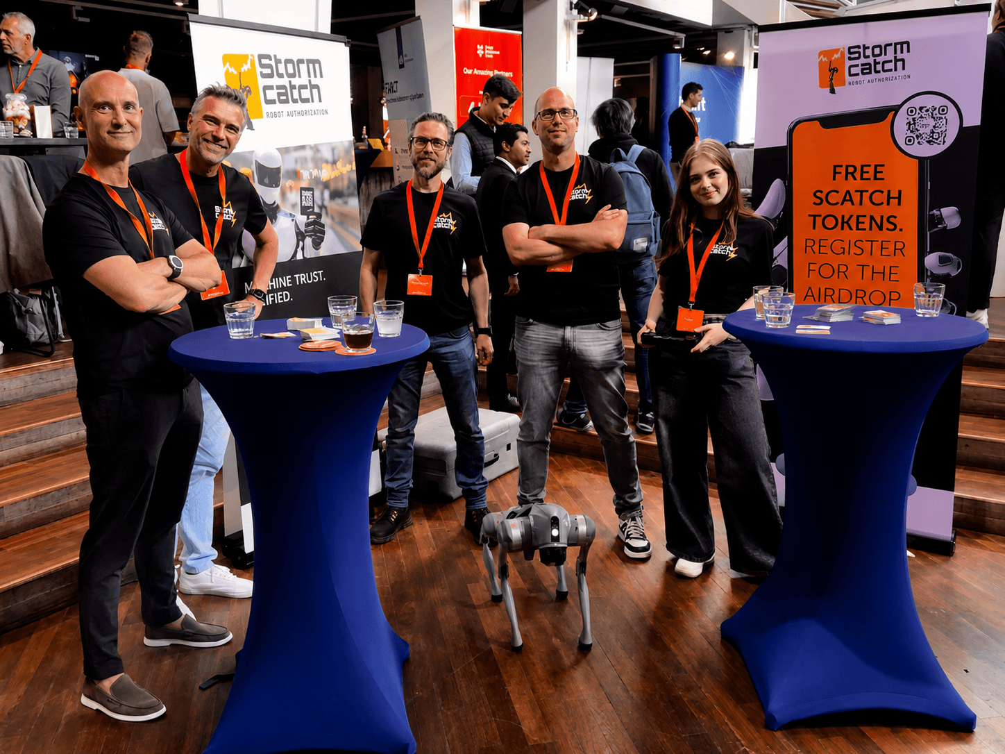 Stormcatch-team rond een robothond bij hightables op een eventbooth, met bezoekers en bannerstands op de achtergrond