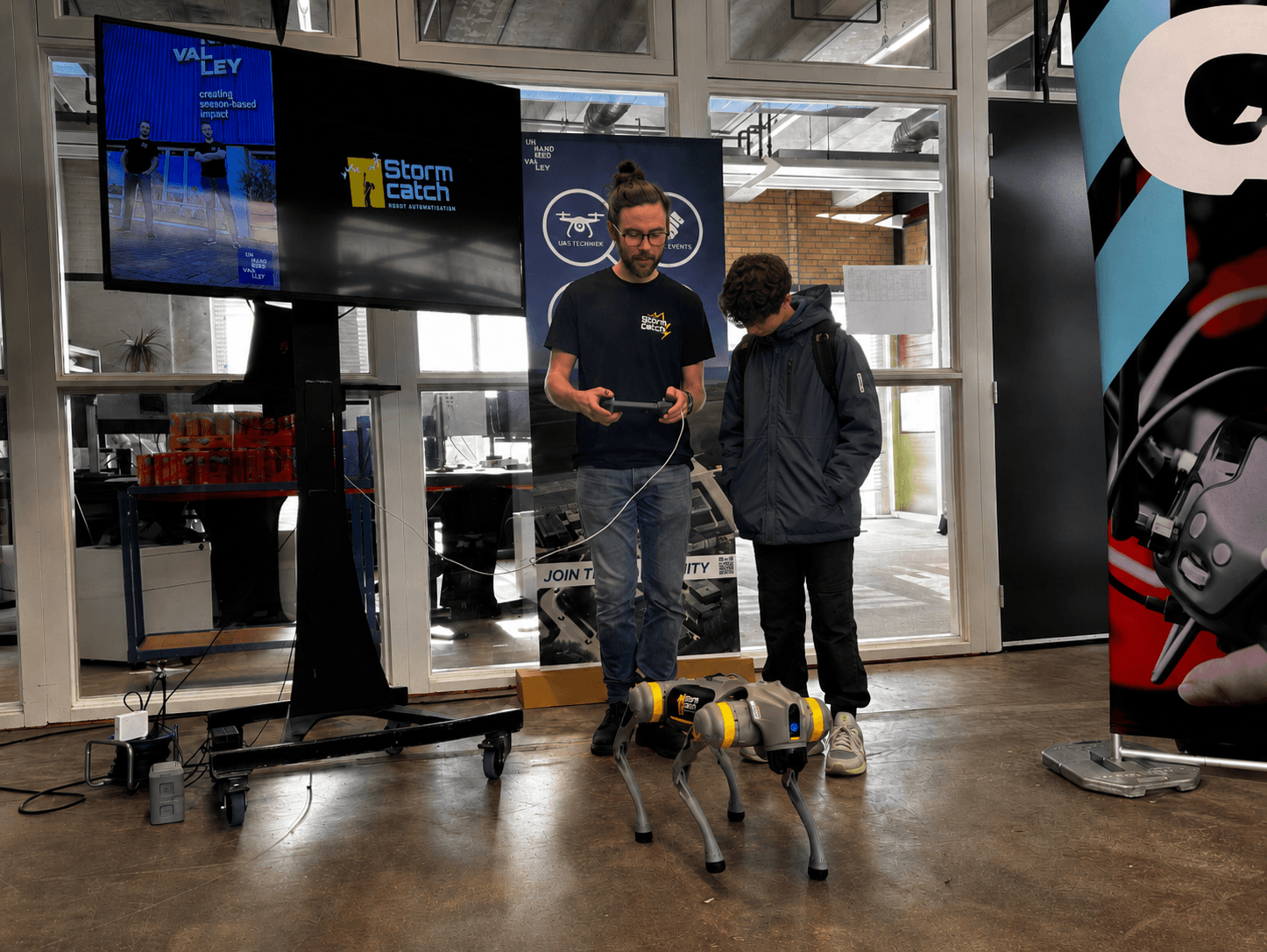 Bezoeker bestuurt zelf een robothond met een controller tijdens een hands-on sessie, met een toeschouwer op de achtergrond