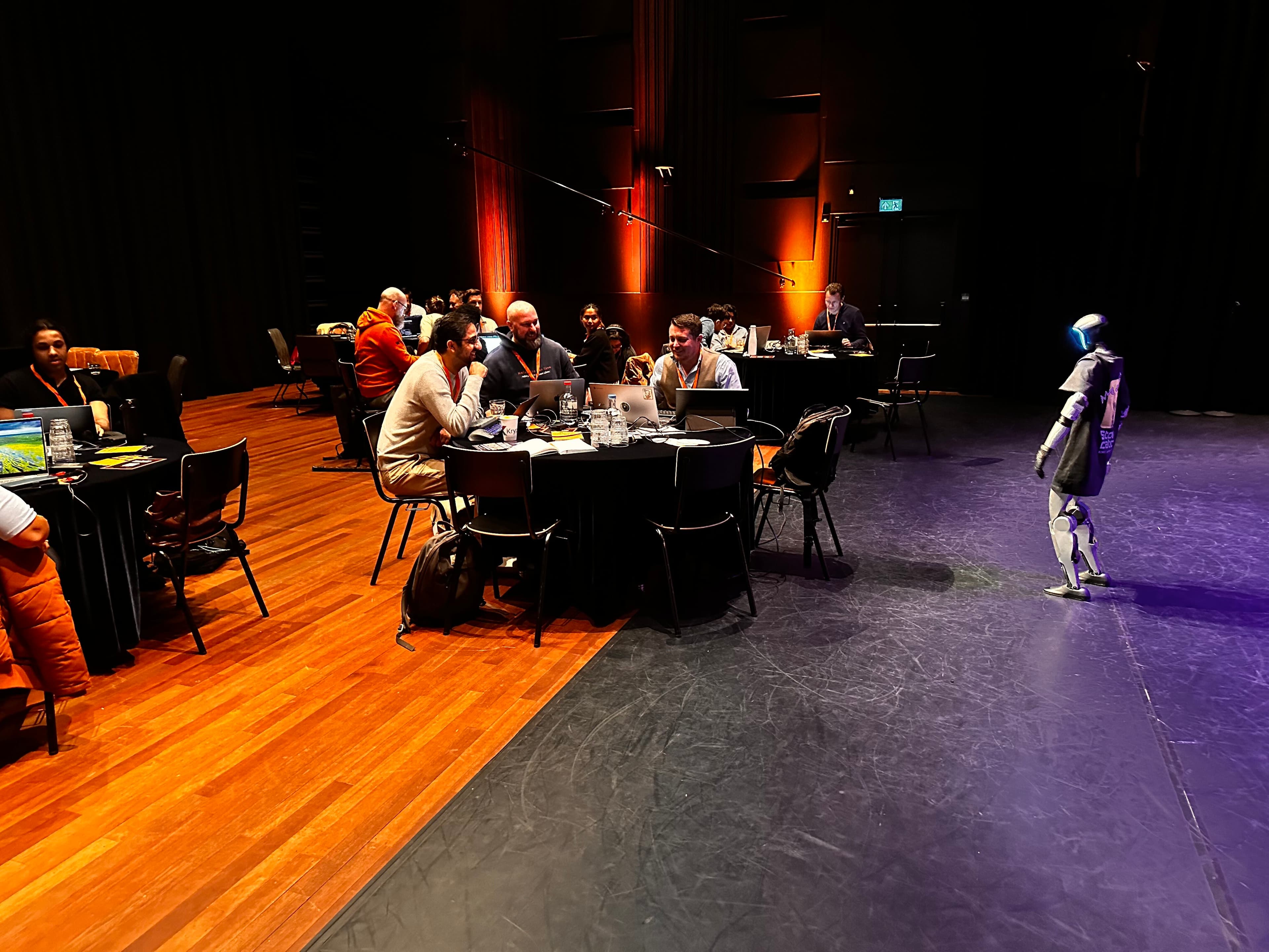 Donkere eventzaal met tafels waar een robot tussen het publiek staat tijdens een podiumshow